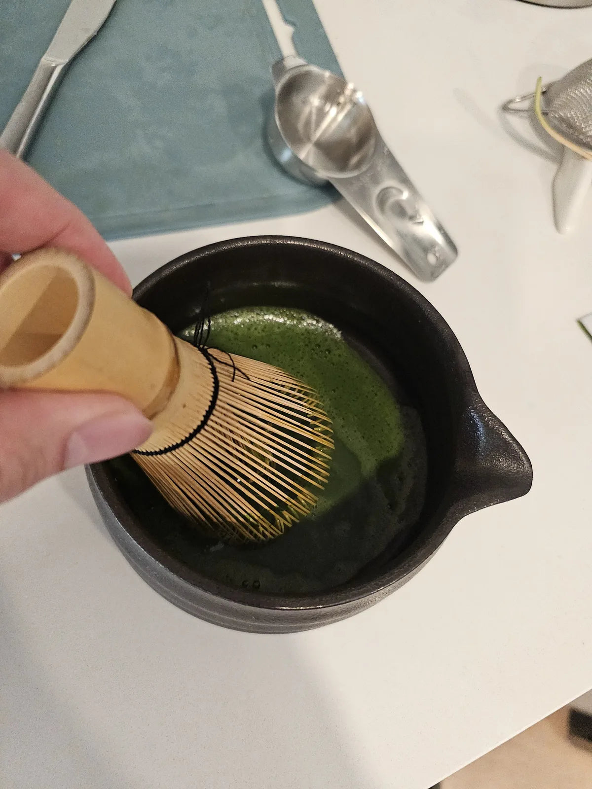 Hand whisking matcha with a bamboo chasen in a ceramic bowl